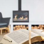A man holding a Bible with a pencil, against the background of the living room with a fireplace. Reading a book in a cozy environment.
